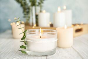 Small white candles in front of a green plant on a wooden surface