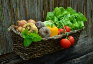 Wicker basket of vegetables, including tomatoes, bell pepper, roots, and leafy greens